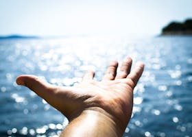 A hand reaching towards the sparkling sea, symbolizing freedom and hope.