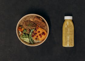 A vibrant vegan bowl with quinoa, fresh vegetables, and a smoothie bottle against a dark backdrop.
