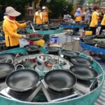 Outdoor market scene with vendors in vibrant attire preparing food at multiple cooking stations.