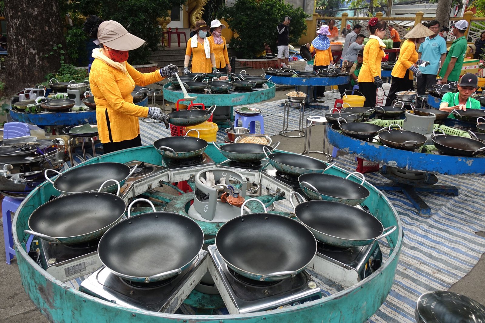 Outdoor market scene with vendors in vibrant attire preparing food at multiple cooking stations.